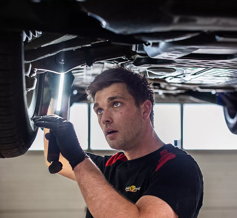 Bilmekaniker hos Syreveien Auto som utfører en kontroll under en bil med lys